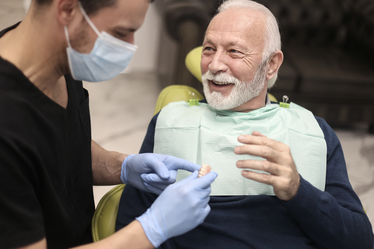 A visit to the dentist Senior man at a dentist's office, looking at dentures. About 65 years old, Caucasian male.